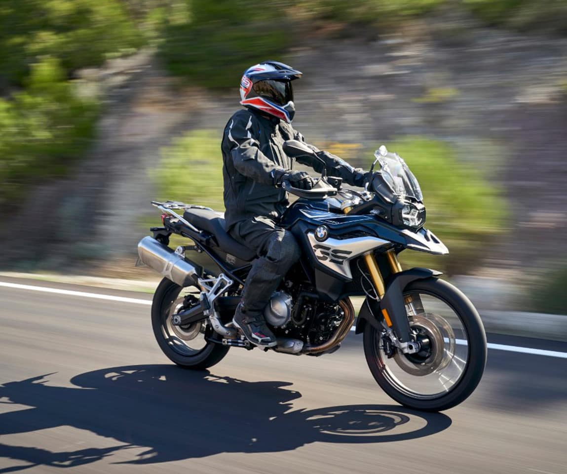 A rider in full gear on a BMW GS motorcycle cruising along a scenic road, capturing the adventure of motorbike touring in Greece and the Balkans.