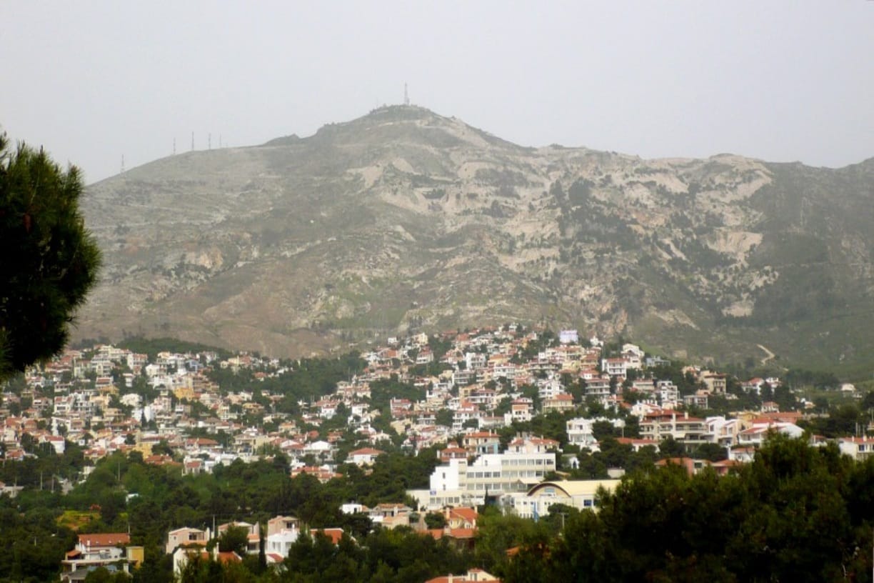 Μια γραφική θέα μιας κατοικημένης πόλης φωλιασμένης στους πρόποδες ενός μεγάλου, απόκρημνου βουνού, ιδανικό για περιπέτειες με μοτοσικλέτες στην Ελλάδα.