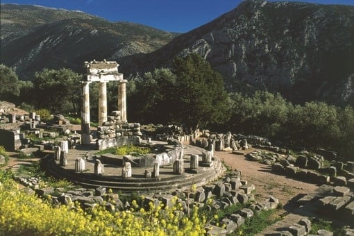 The Tholos of Delphi, an ancient circular temple ruin in Greece, set against a backdrop of rugged mountains during a motorcycle adventure tour.