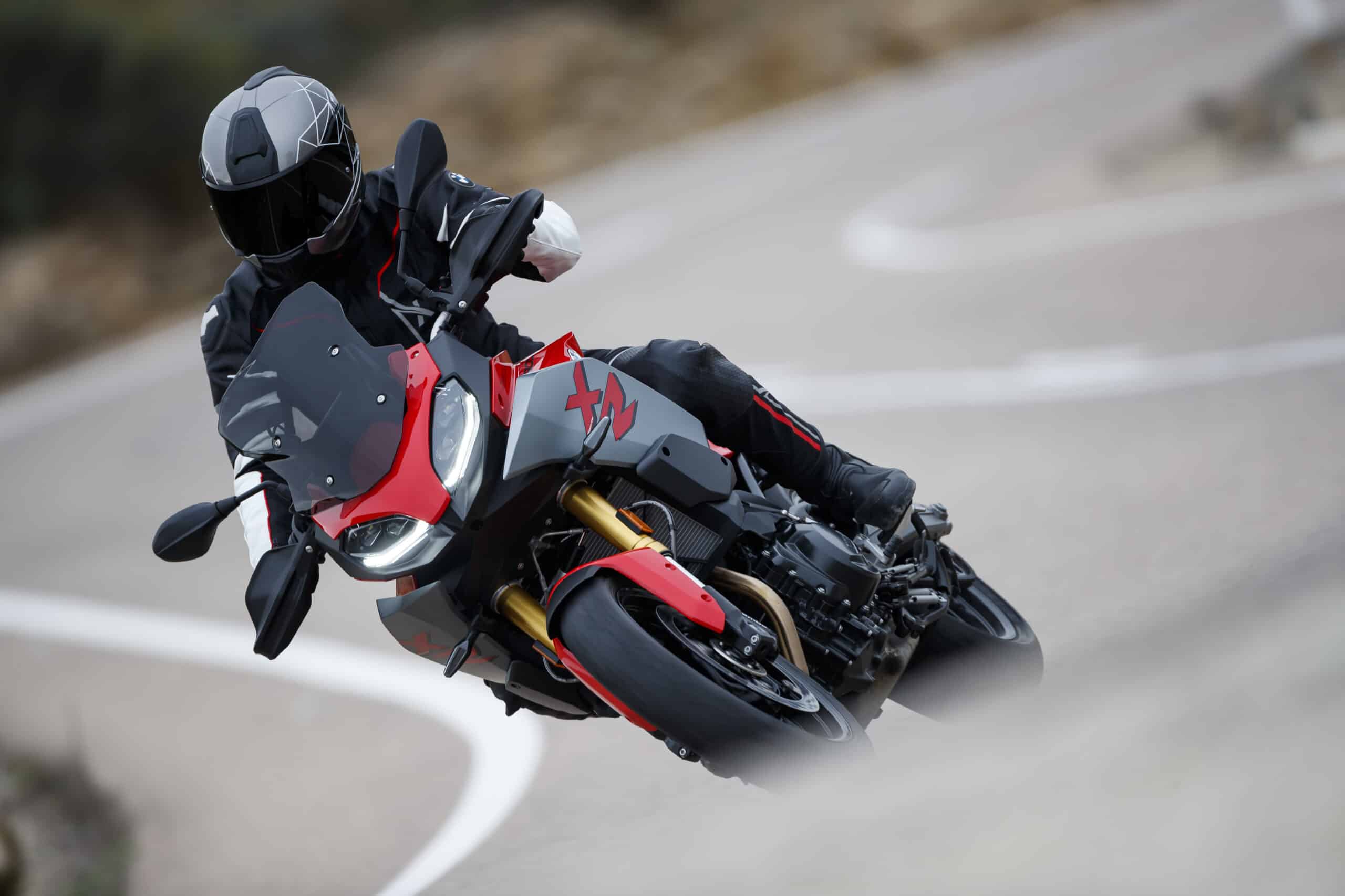 A rider in full gear leans a red and grey BMW motorcycle into a curve on a winding mountain road, showcasing a dynamic motorcycle rental experience.