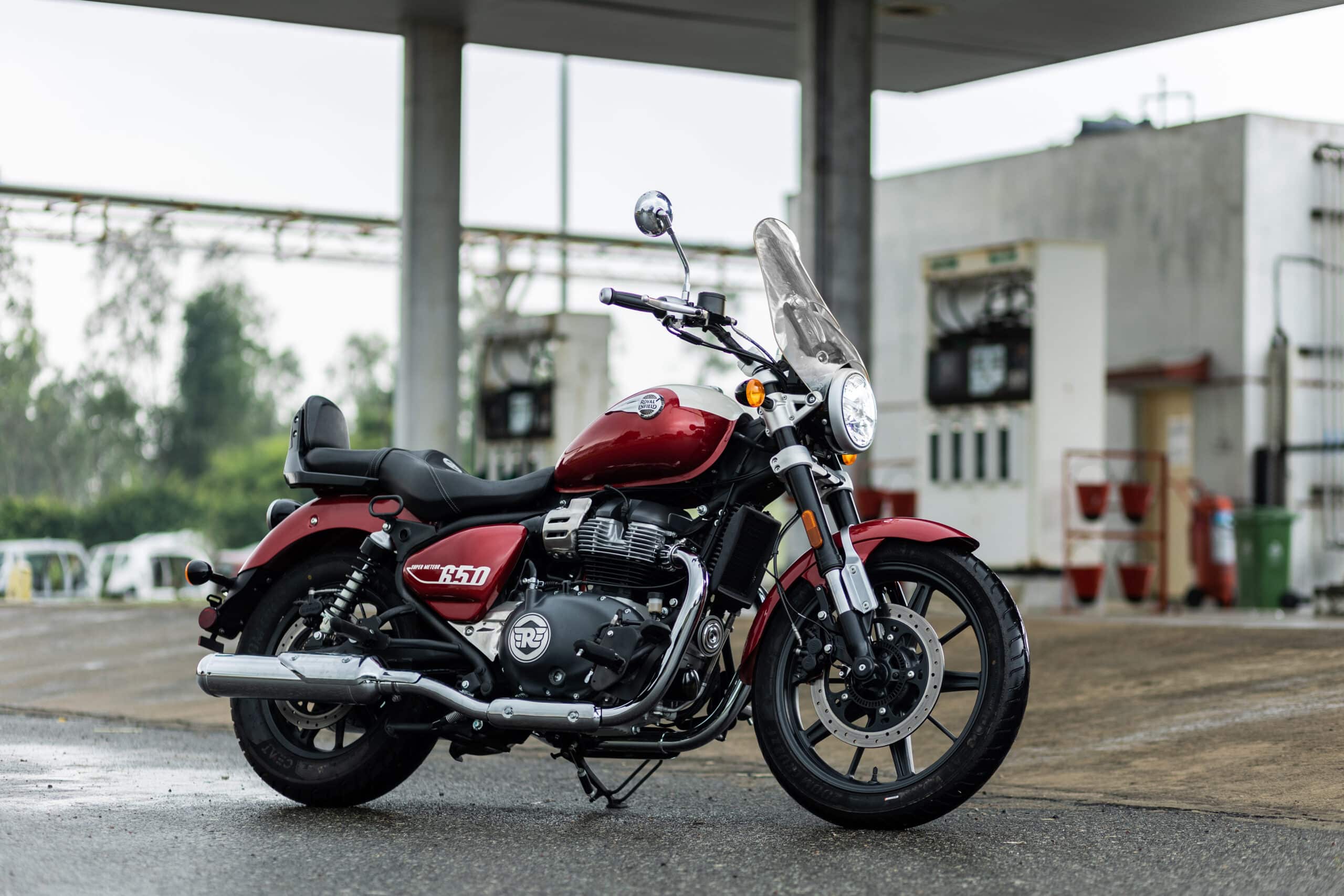 A red and silver Royal Enfield Super Meteor 650 cruiser motorcycle parked at a gas station, ready for a motorcycle tour adventure in Greece.