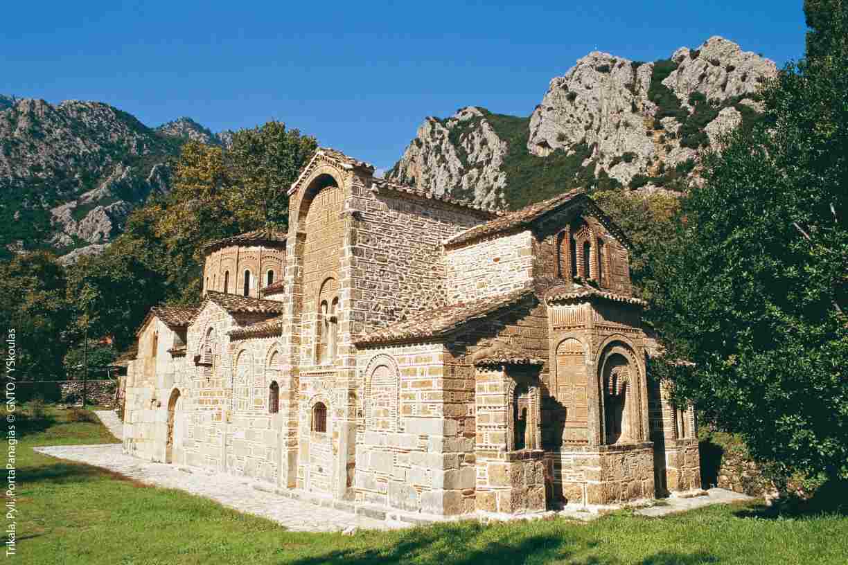 The historic stone Byzantine church of Porta Panagia in Pyli, Greece, set against a backdrop of rugged mountains during a motorcycle adventure tour.