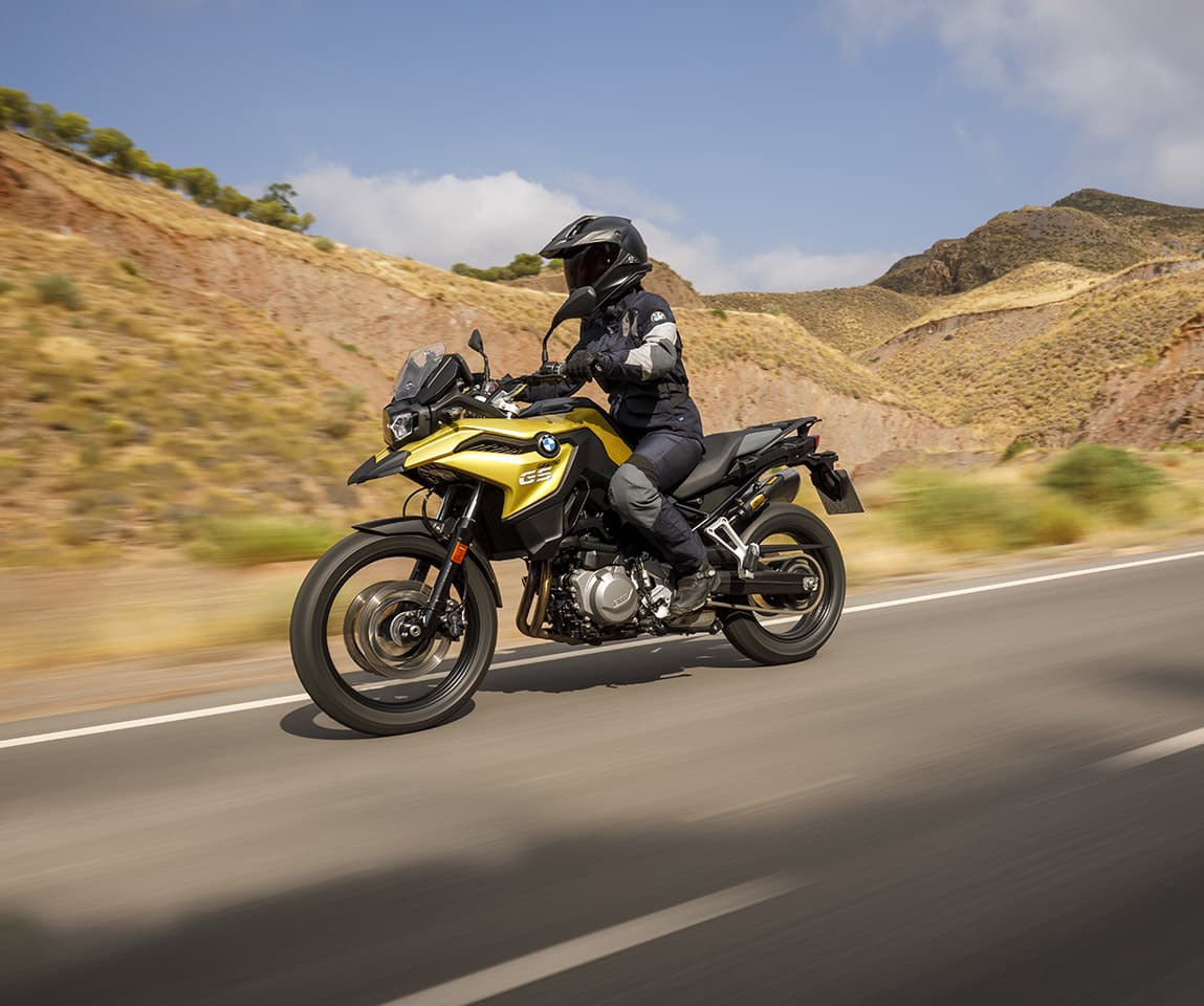 A rider on a yellow BMW GS motorcycle cruising along a scenic mountain road, representing a motorcycle adventure rental experience in Greece.