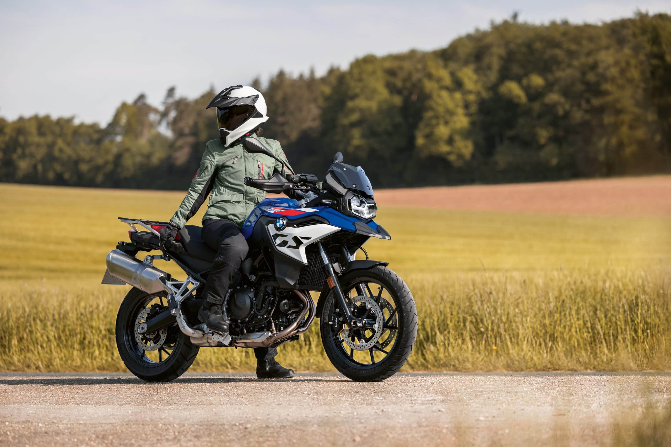 A rider in protective gear sits on a blue and white BMW GS motorcycle on a rural road, ready for a motorcycle adventure tour in Greece.