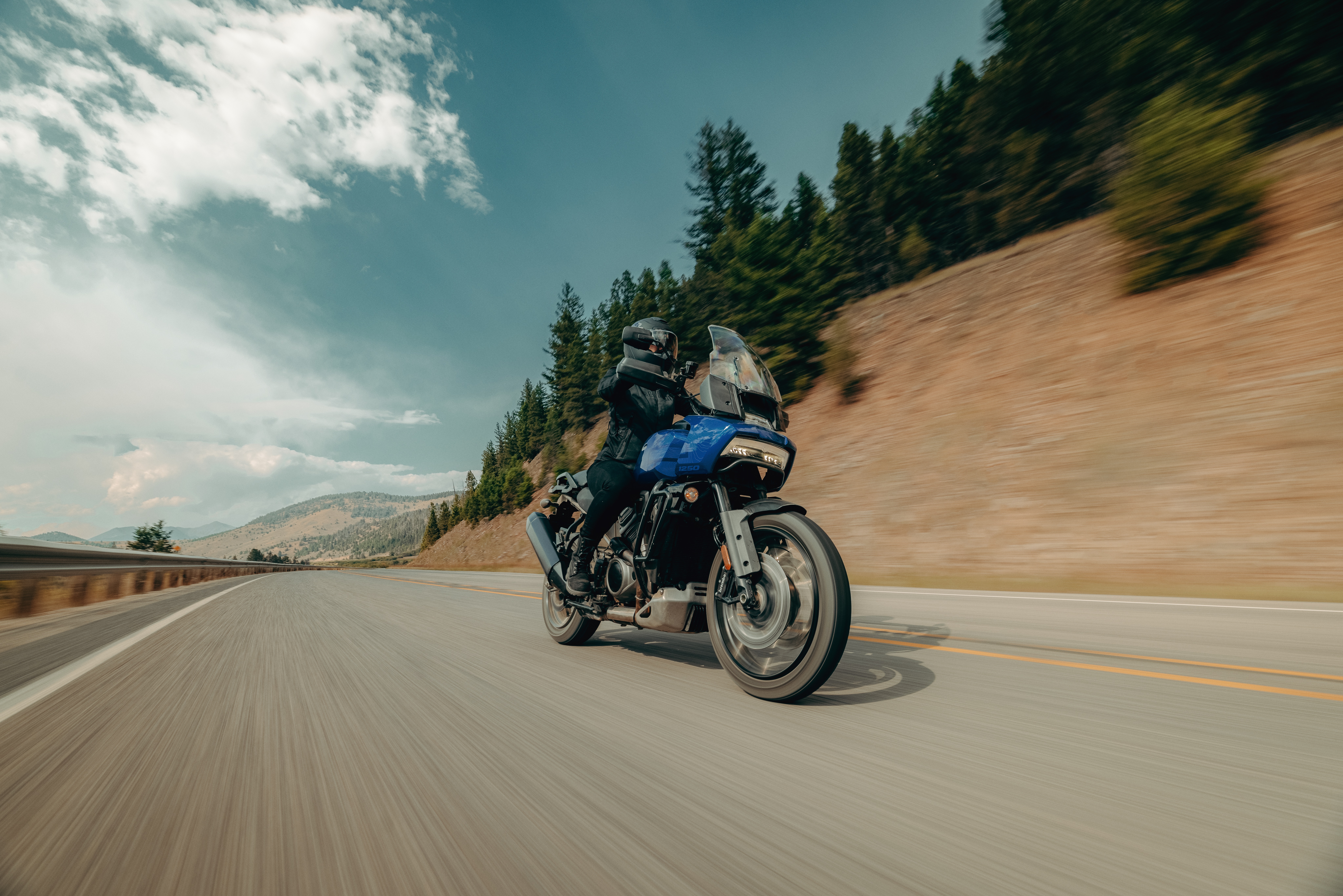 A rider on a blue adventure motorcycle cruising along a scenic mountain road, showcasing the thrill of motorbike touring in Greece and the Balkans.