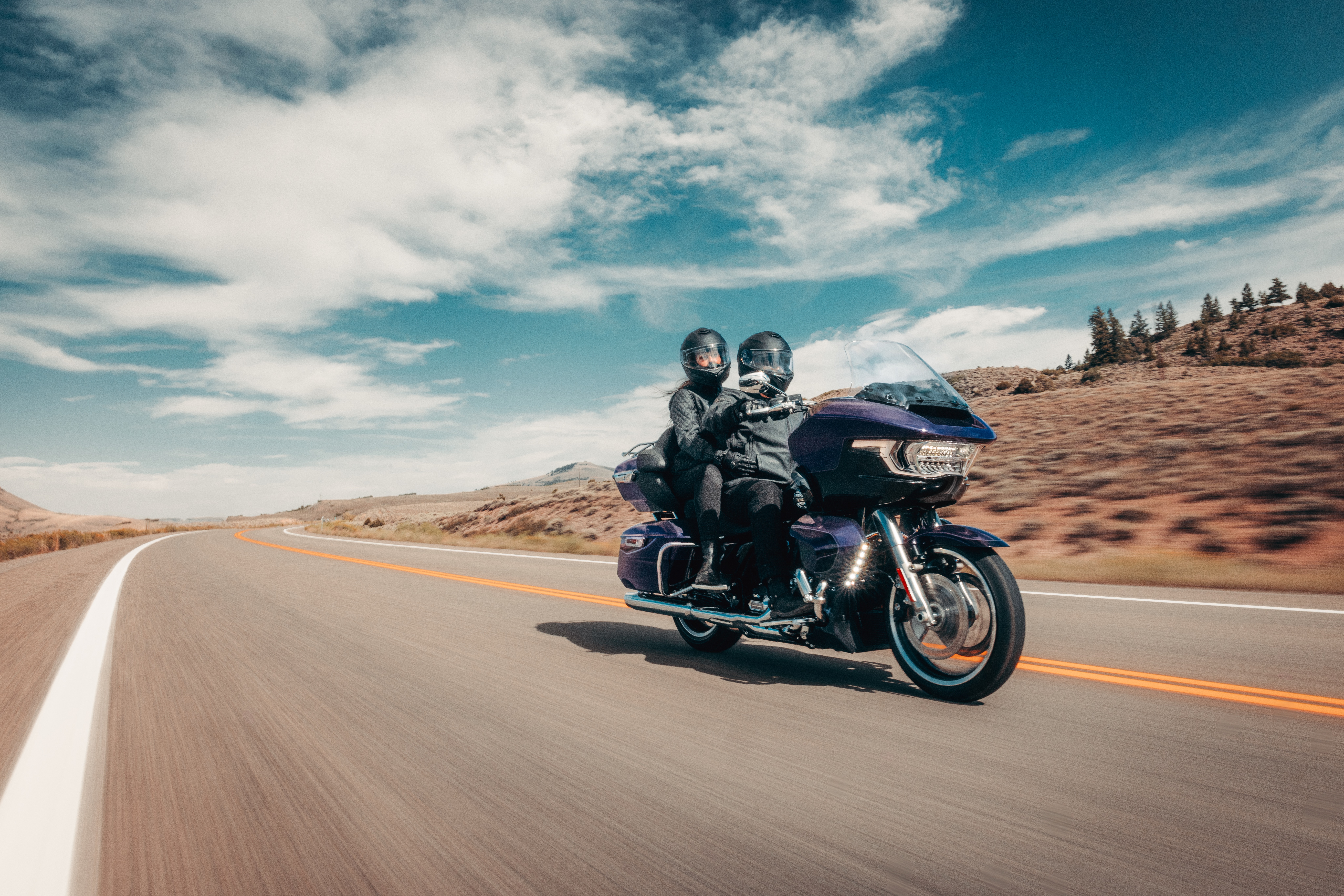 Two people wearing helmets riding a purple touring motorcycle on a scenic open road during a motorcycle adventure tour in Greece.